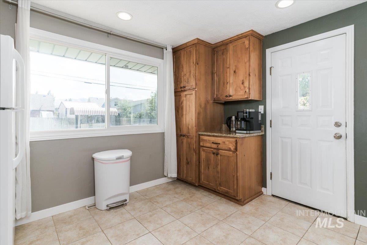 Kitchen featuring light stone countertops, brown cabinetry, freestanding refrigerator, and light tile patterned floors