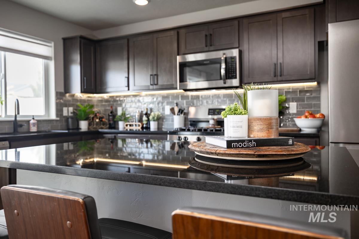 Kitchen with stainless steel appliances, tasteful backsplash, dark brown cabinetry, dark stone counters, and recessed lighting