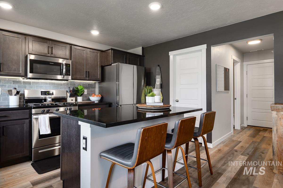 Kitchen featuring stainless steel appliances, a kitchen breakfast bar, a kitchen island, decorative backsplash, and light wood finished floors