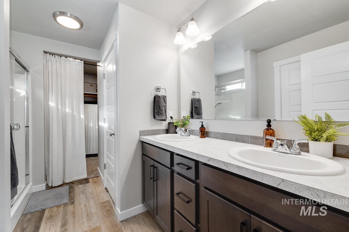 Bathroom featuring a stall shower, double vanity, light wood-style flooring, and a walk in closet