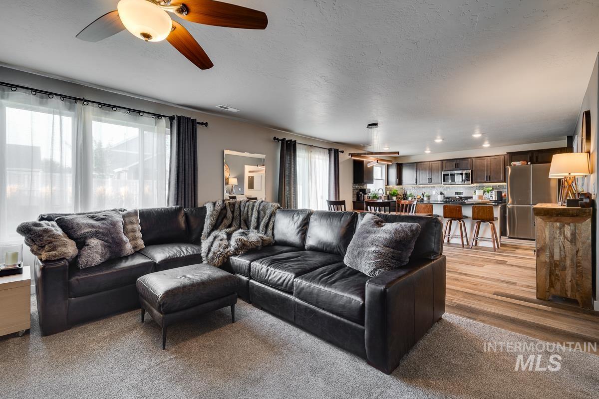 Living room featuring plenty of natural light, a textured ceiling, a ceiling fan, light colored carpet, and light wood-type flooring