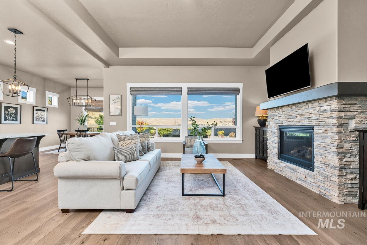 Living area with a raised ceiling, light wood finished floors, and a stone fireplace
