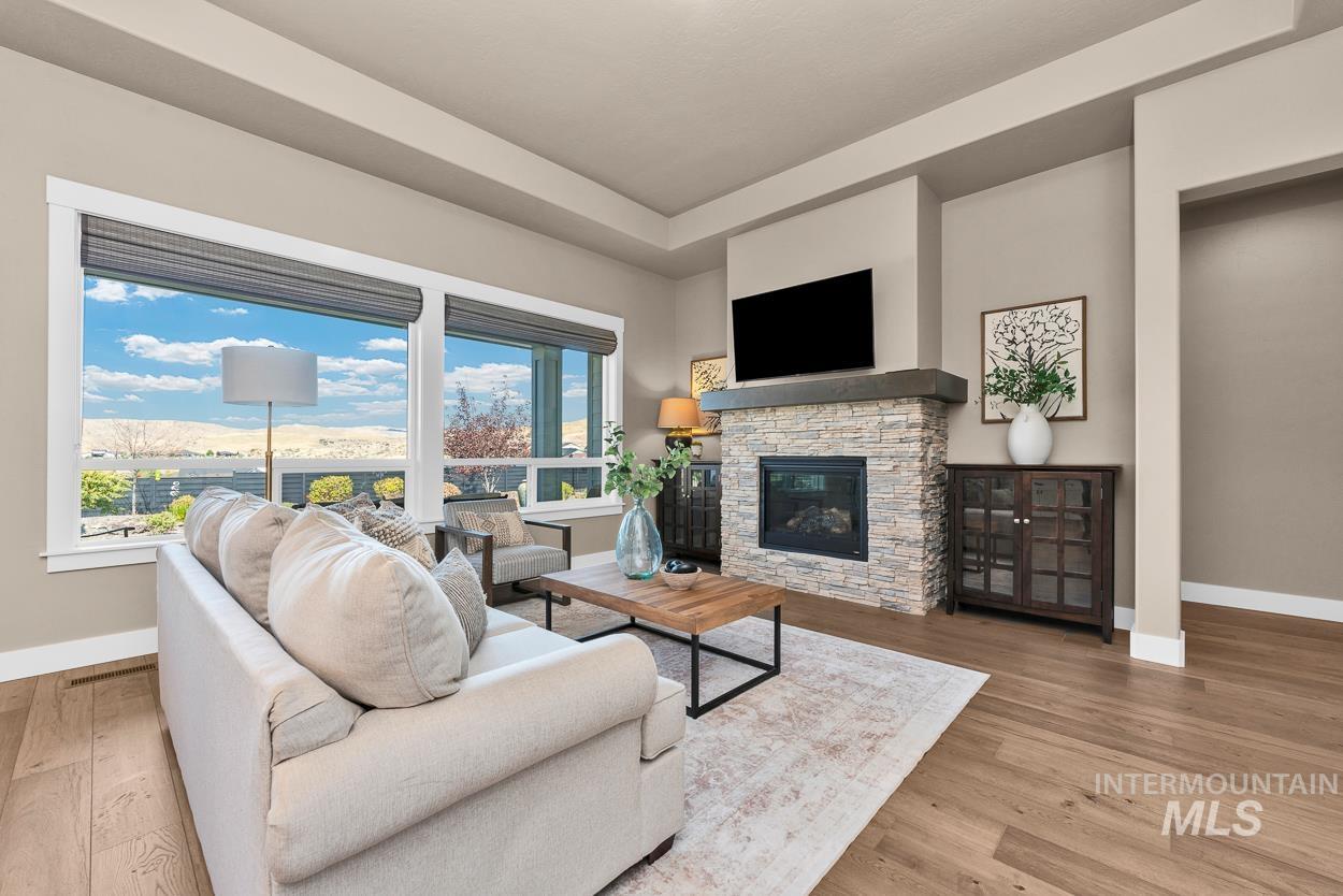 Living room with a stone fireplace, light wood-style flooring, and a tray ceiling