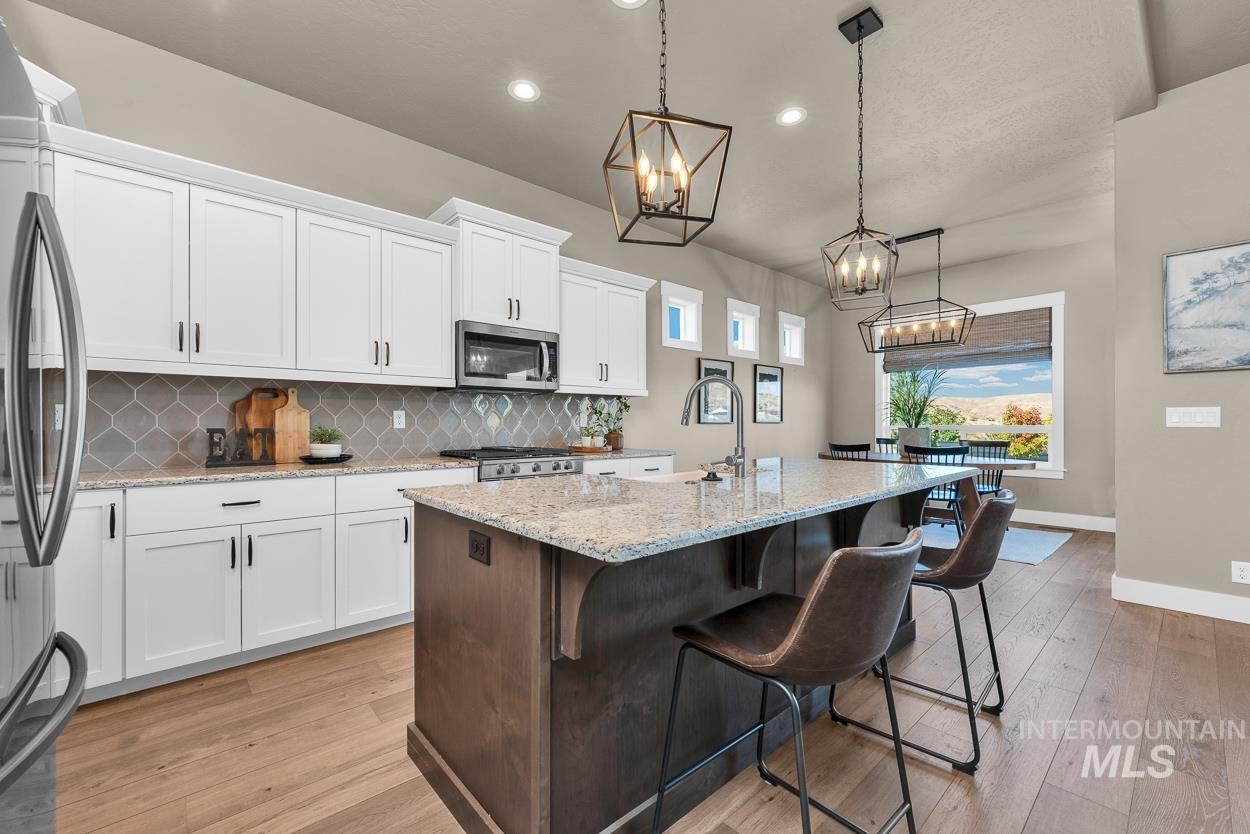 Kitchen with tasteful backsplash, white cabinets, light stone countertops, a breakfast bar area, and an island with sink