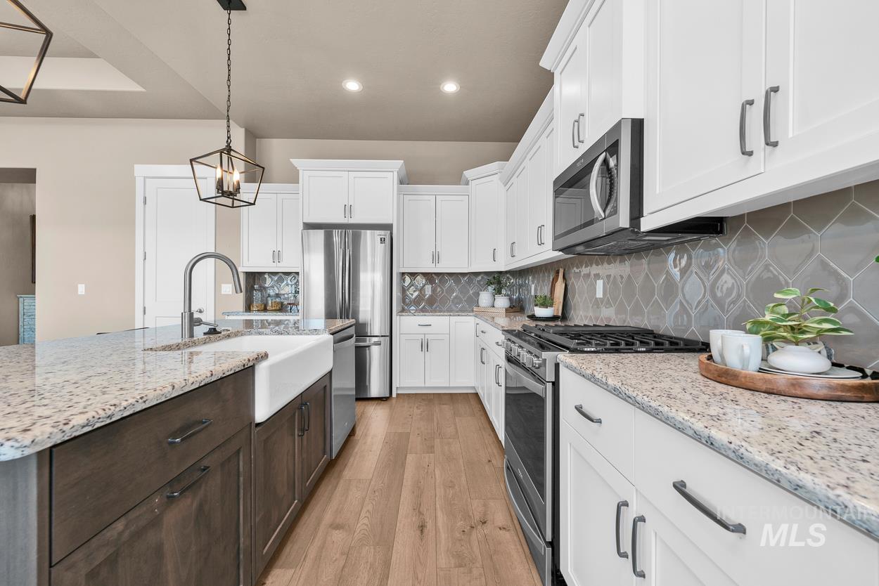 Kitchen featuring stainless steel appliances, backsplash, light wood-type flooring, decorative light fixtures, and light stone counters