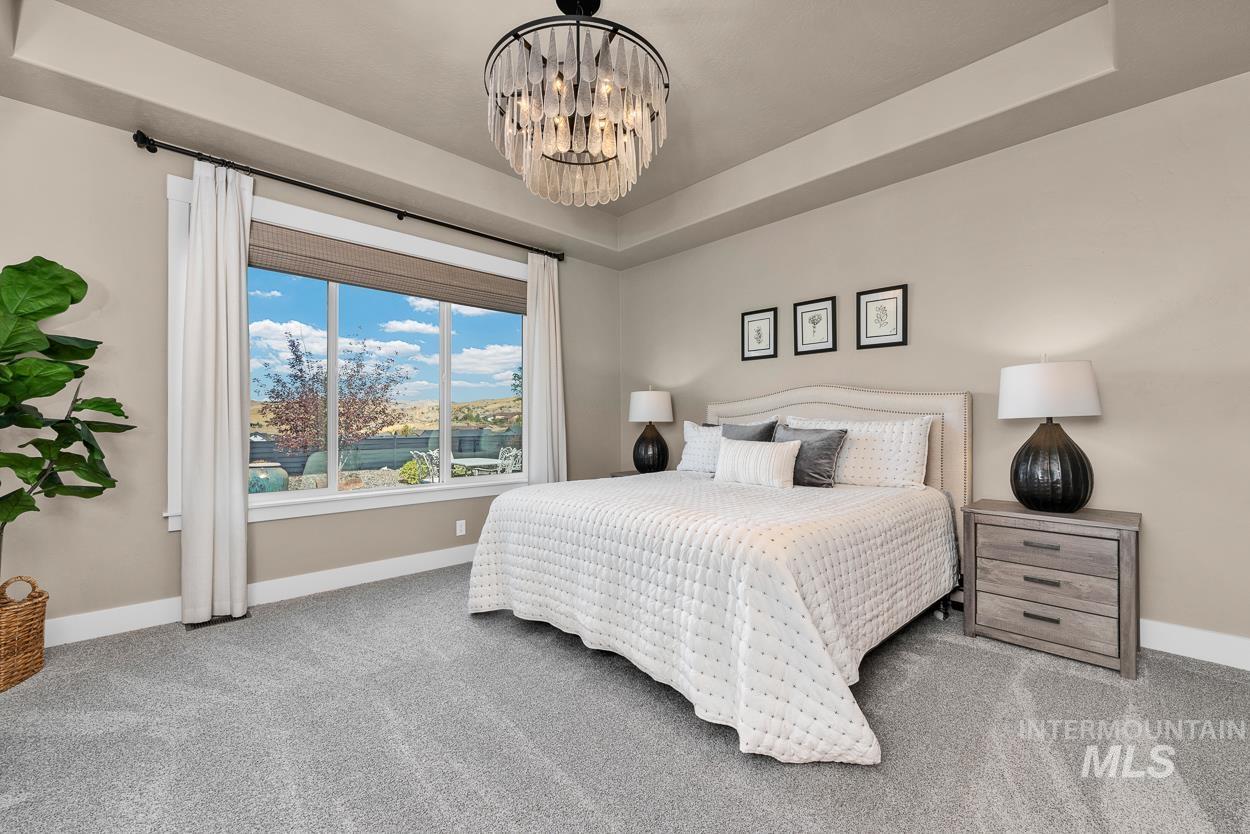 Bedroom with a tray ceiling, light colored carpet, and a chandelier
