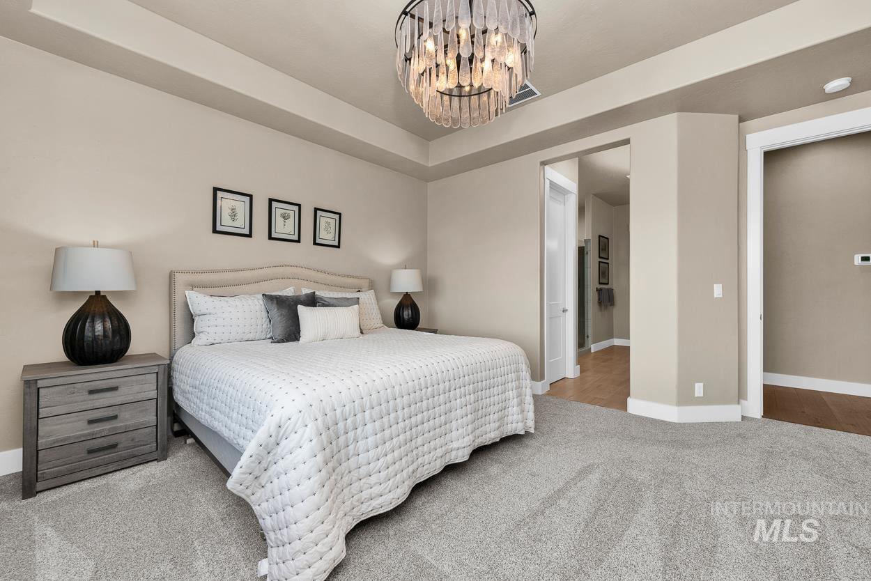 Bedroom with light carpet, a tray ceiling, and a chandelier