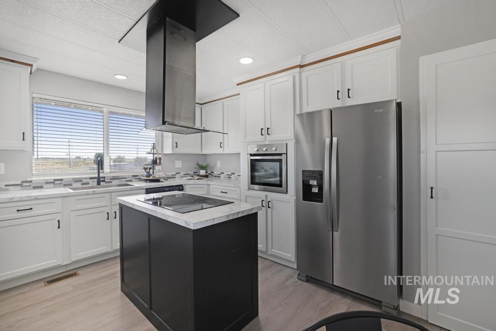 Kitchen with appliances with stainless steel finishes, white cabinets, dark cabinets, a kitchen island, and light wood-style floors