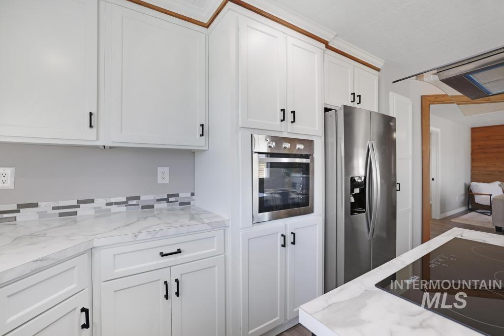 Kitchen featuring appliances with stainless steel finishes, white cabinetry, and light stone countertops