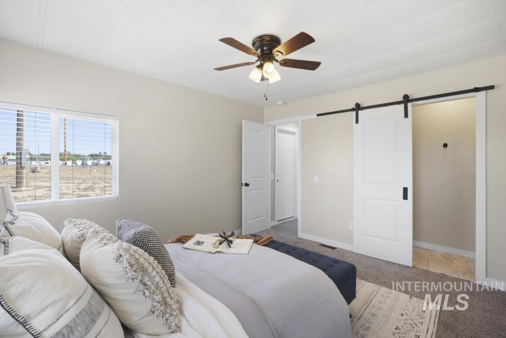 Bedroom with a barn door, carpet floors, and a ceiling fan