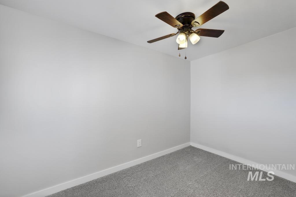 Carpeted empty room featuring baseboards and ceiling fan