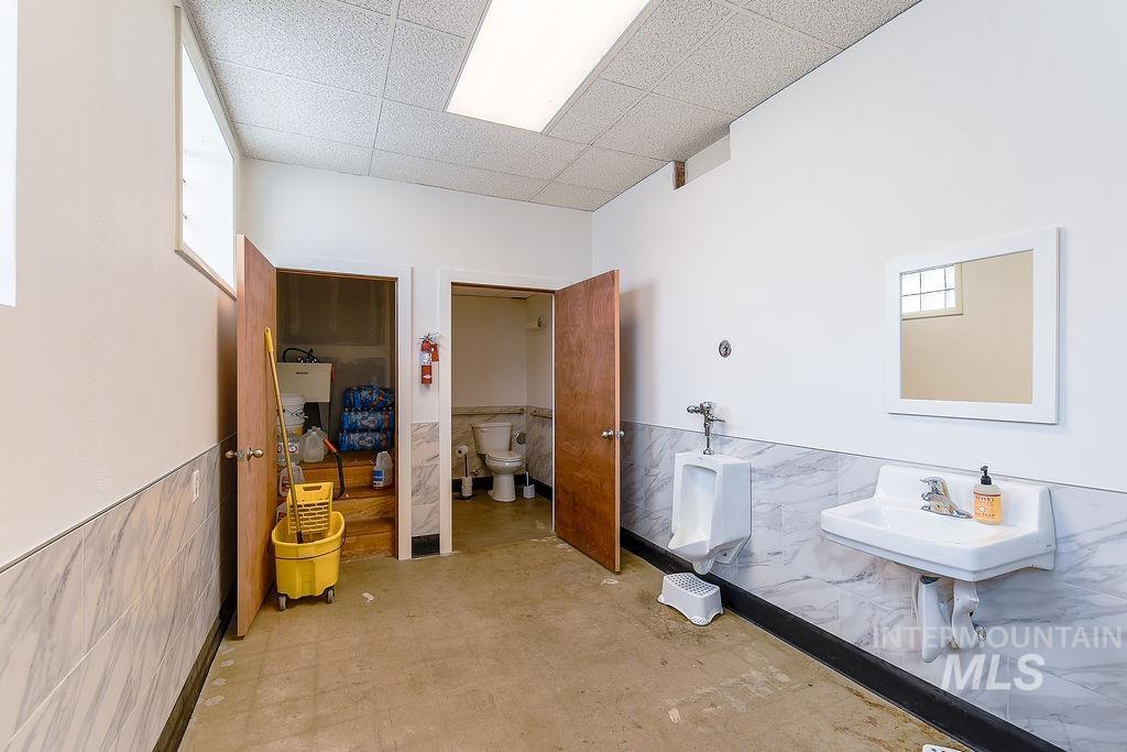 Bathroom with tile walls, wainscoting, a drop ceiling, and light floors