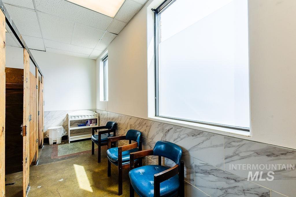 Sitting room with plenty of natural light, wainscoting, a drop ceiling, and tile walls