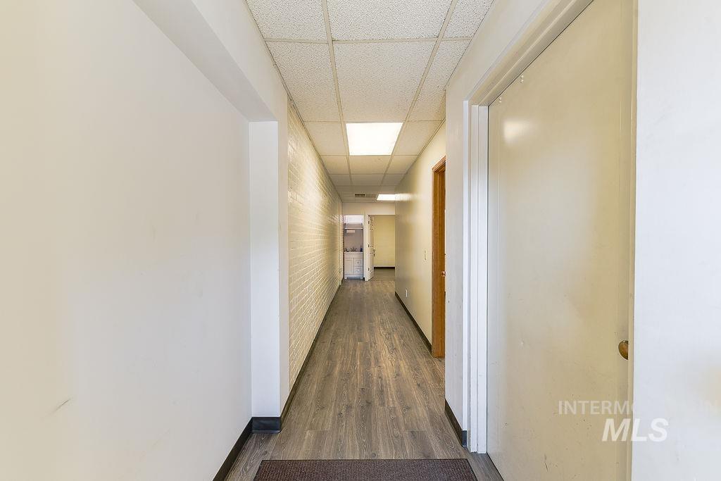 Corridor with a paneled ceiling, dark wood-type flooring, and brick wall