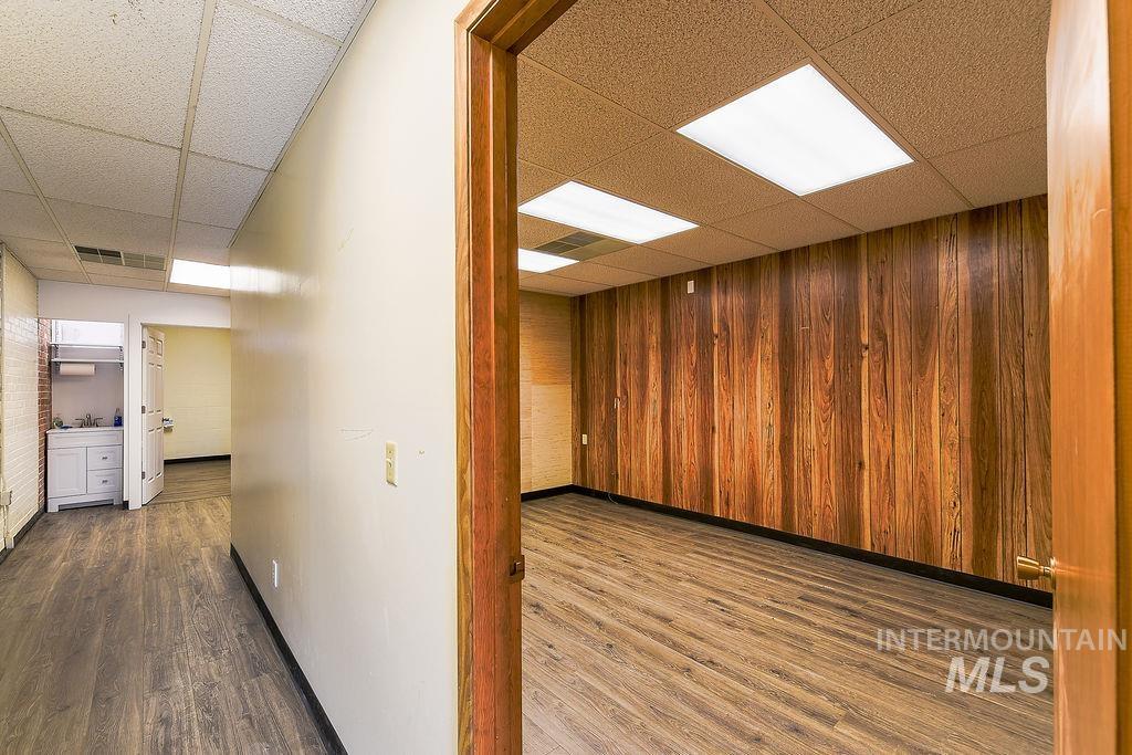Corridor with a drop ceiling, dark wood-style flooring, and wooden walls