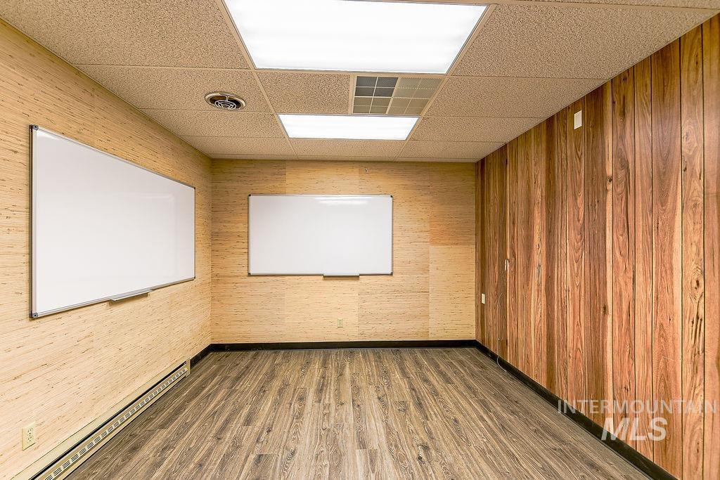 Empty room featuring dark wood finished floors, a drop ceiling, and baseboard heating