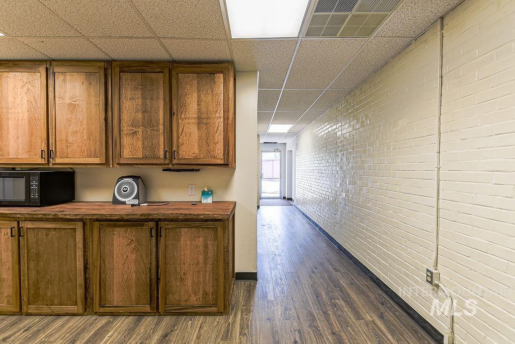 Corridor featuring a paneled ceiling, dark wood-style floors, and brick wall