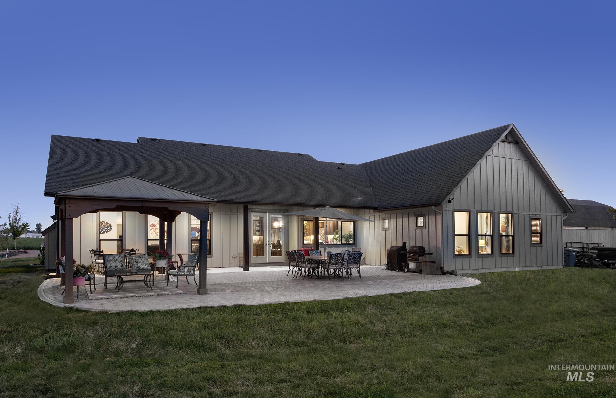 Back of property featuring board and batten siding, a patio area, roof with shingles, and a yard