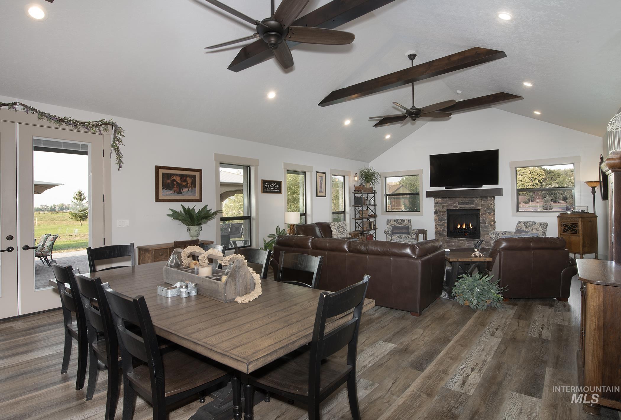 Dining area featuring beam ceiling, french doors, a stone fireplace, ceiling fan, and dark wood finished floors