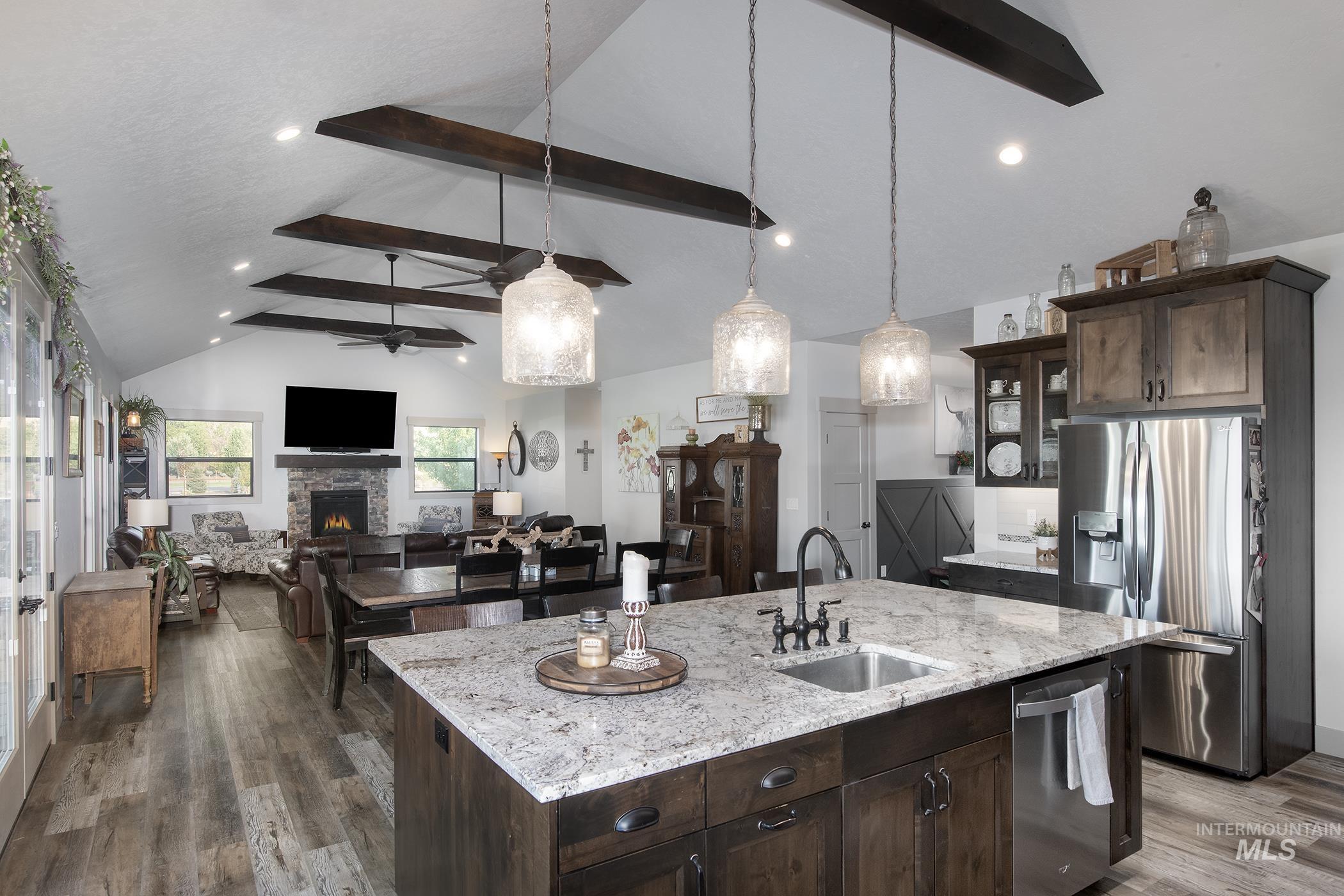 Kitchen featuring dark brown cabinetry, beamed ceiling, stainless steel appliances, a fireplace, and light stone countertops