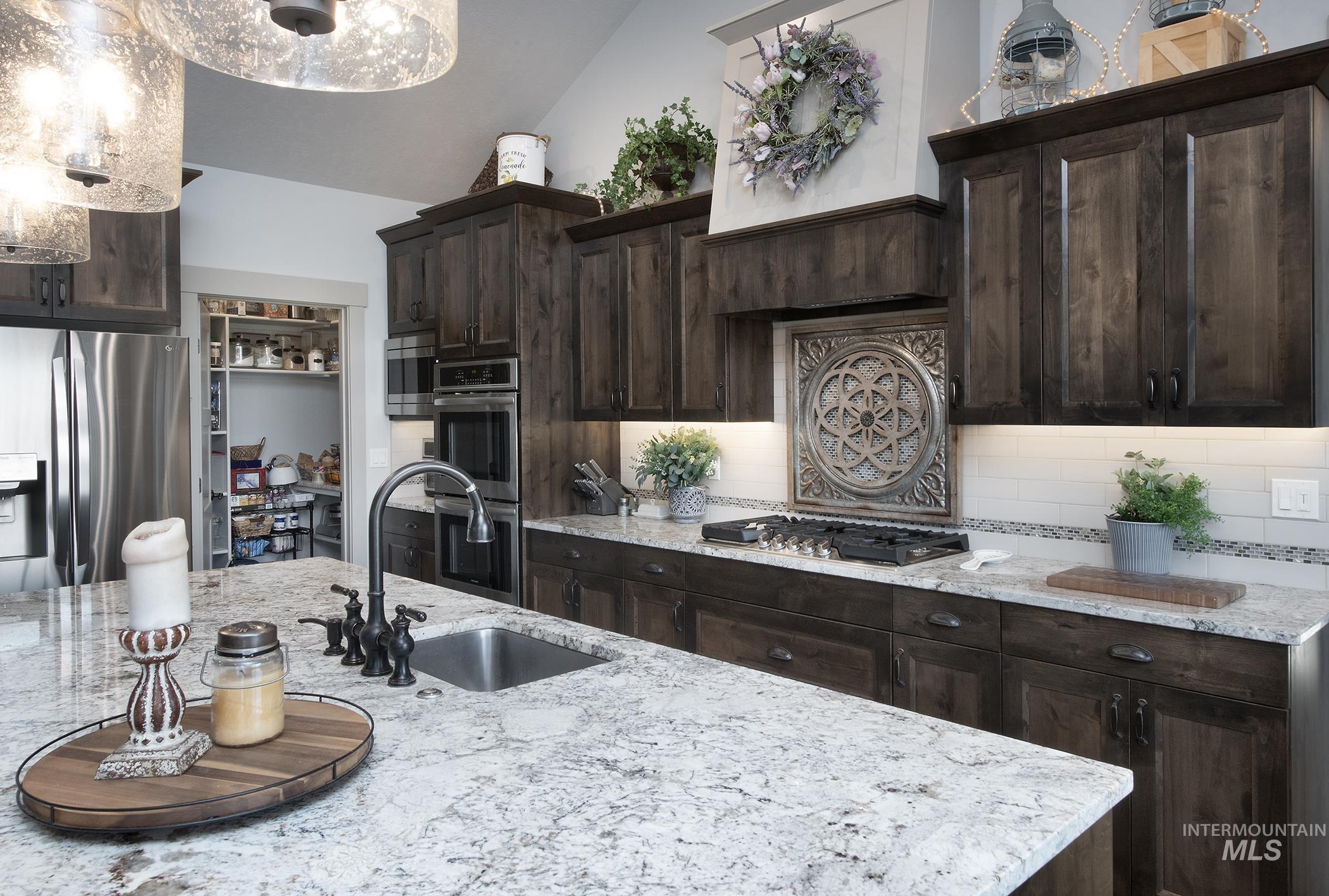 Kitchen featuring dark brown cabinetry, appliances with stainless steel finishes, decorative backsplash, light stone counters, and vaulted ceiling