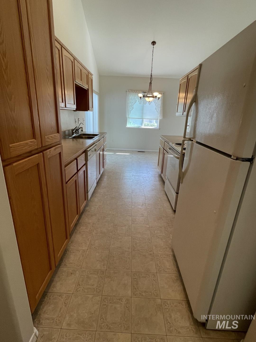 Kitchen featuring white appliances, hanging light fixtures, brown cabinets, lofted ceiling, and a chandelier