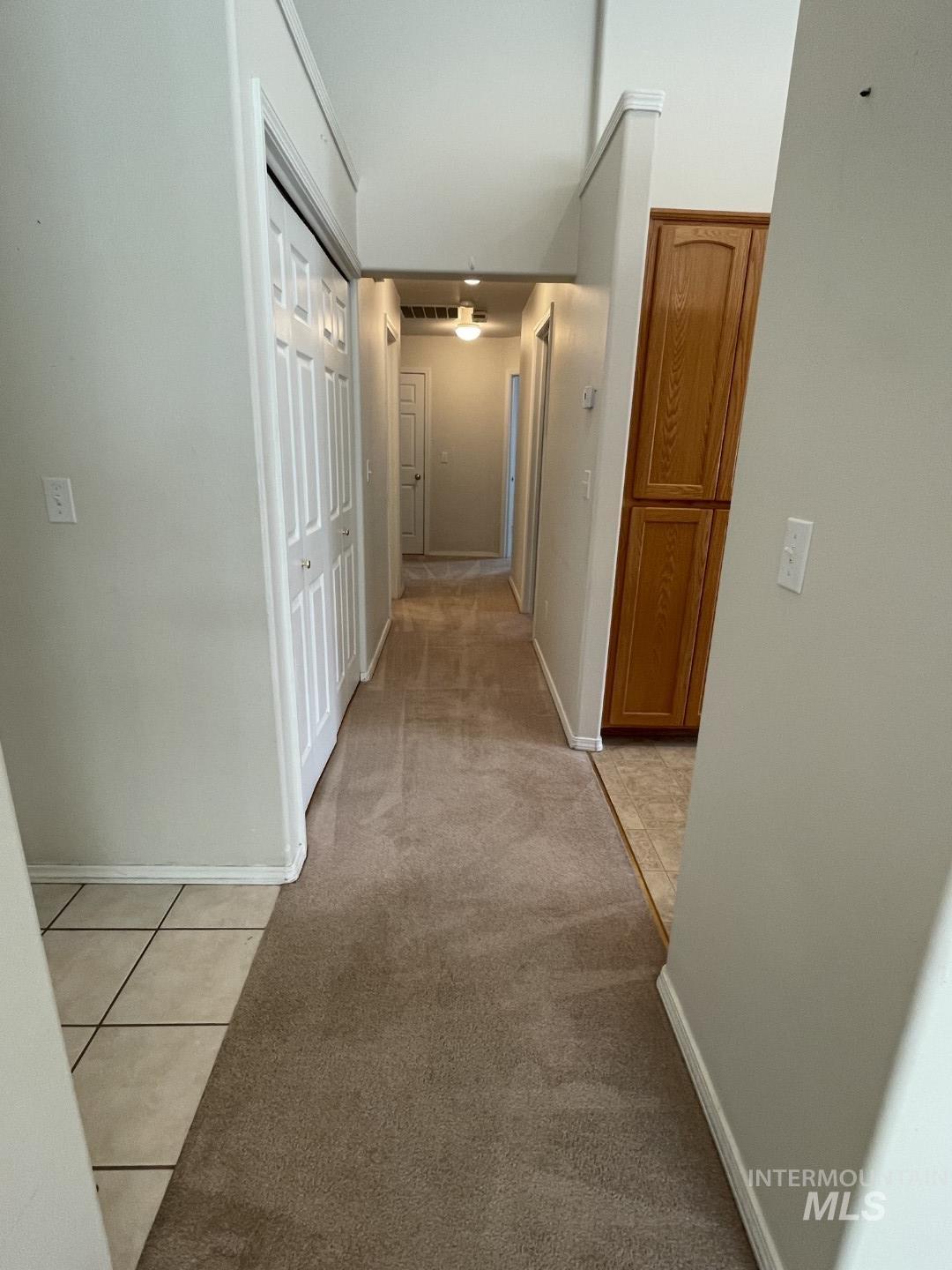 Corridor with light tile patterned floors and light colored carpet