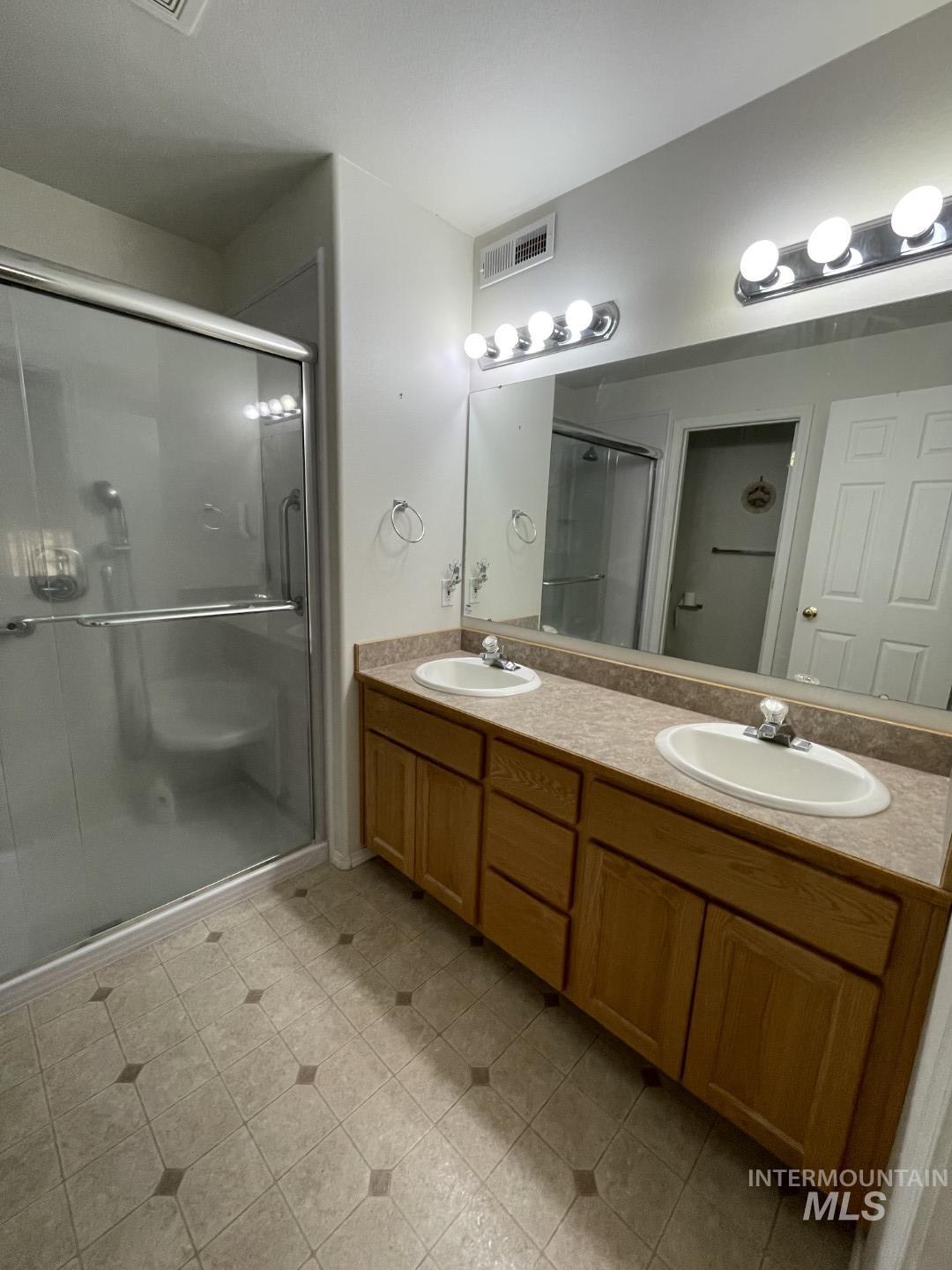Full bath featuring a shower stall, double vanity, and light tile patterned floors