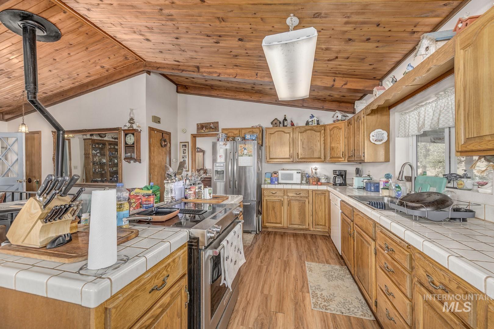 Kitchen featuring appliances with stainless steel finishes, light wood-type flooring, tile countertops, brown cabinets, and wood ceiling