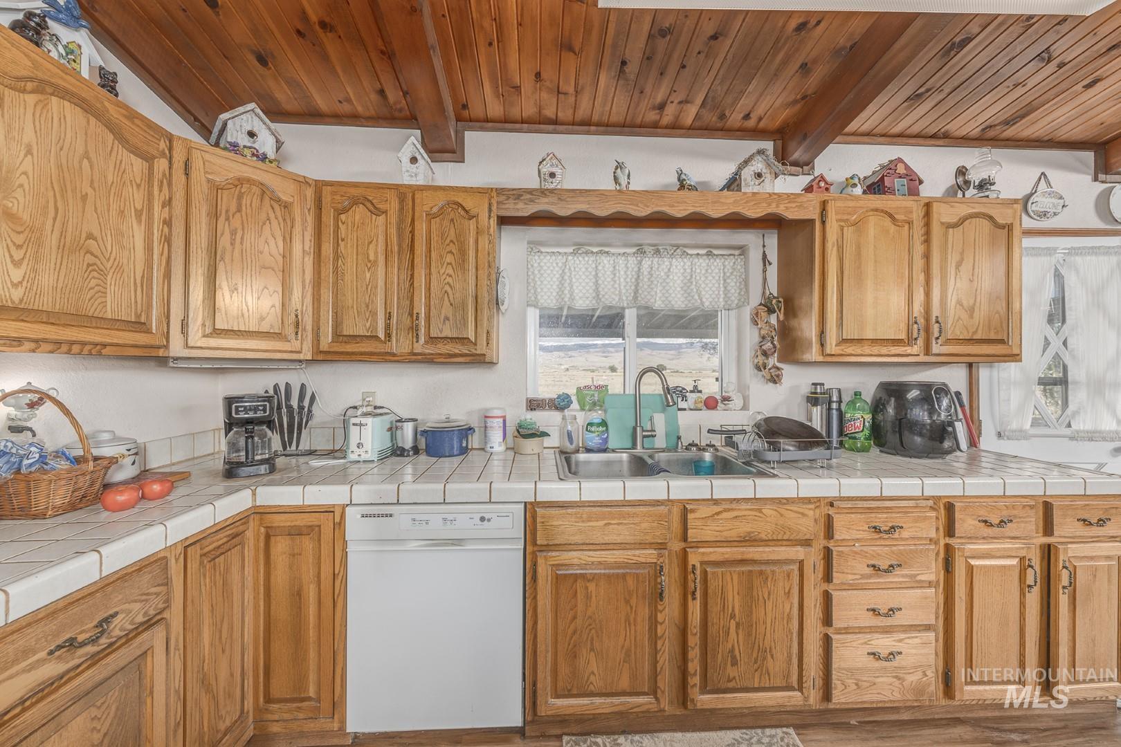 Kitchen featuring beam ceiling, dishwasher, tile counters, and brown cabinetry
