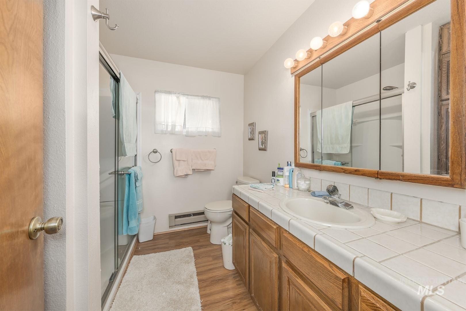 Full bath with vanity, dark wood finished floors, a shower stall, and a baseboard radiator