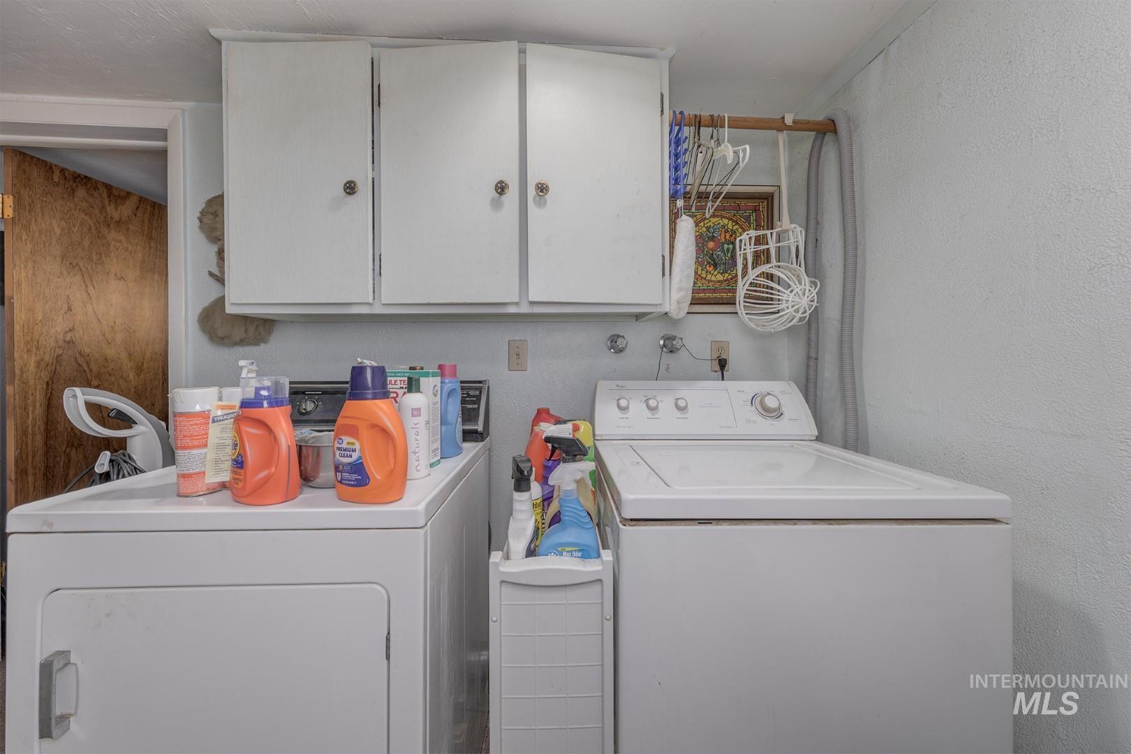 Washroom with a textured wall, washer and dryer, and cabinet space