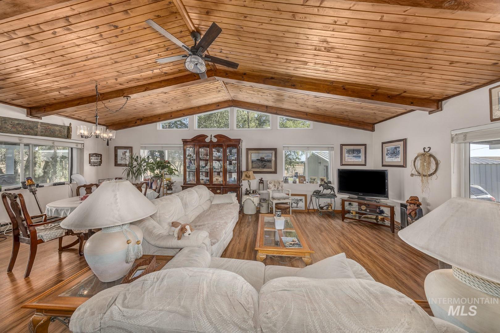 Living area with a wooden ceiling with exposed beams, wood finished floors, ceiling fan, a chandelier, and high vaulted ceiling