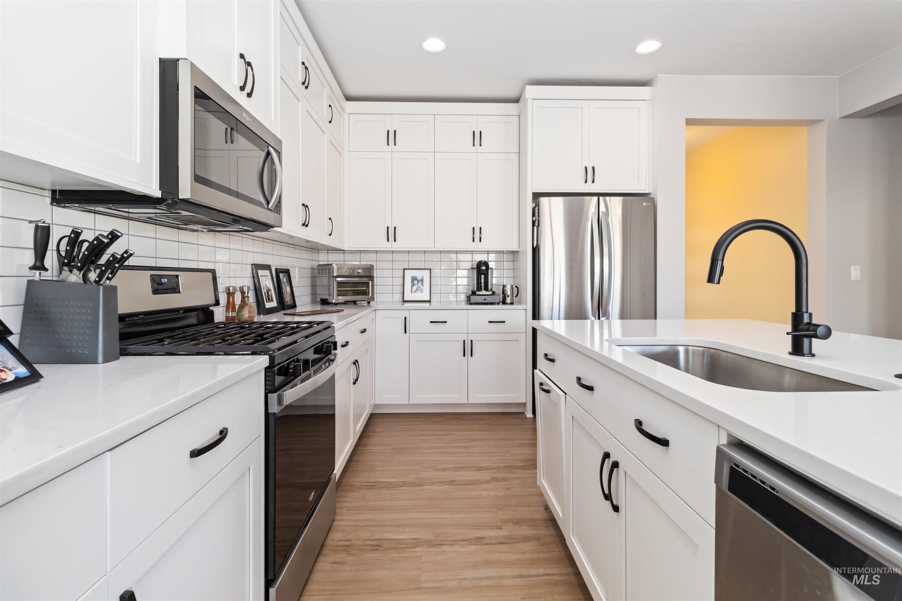Kitchen featuring appliances with stainless steel finishes, white cabinets, decorative backsplash, light stone countertops, and recessed lighting