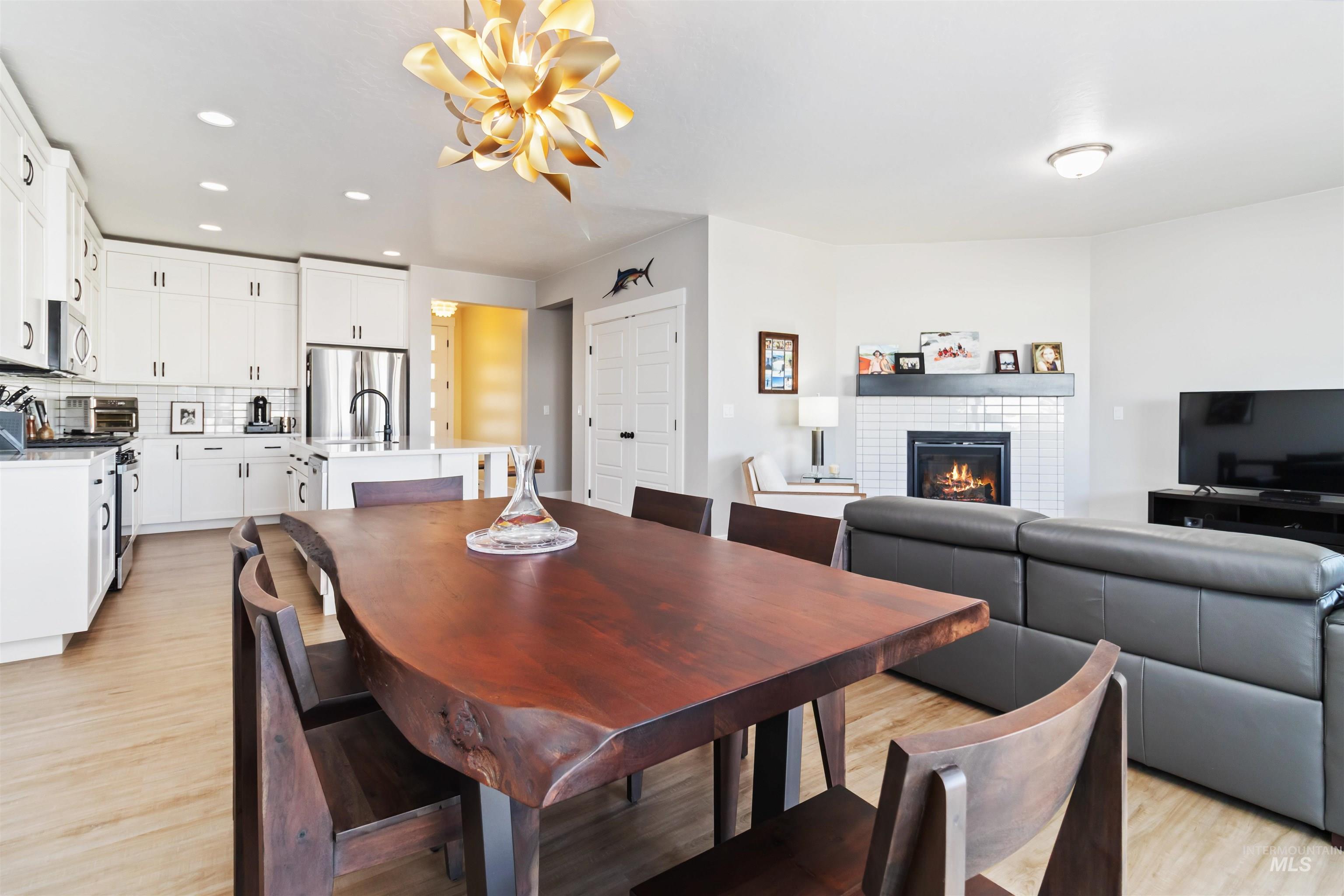 Dining area featuring a tiled fireplace, light wood-style flooring, recessed lighting, and a chandelier