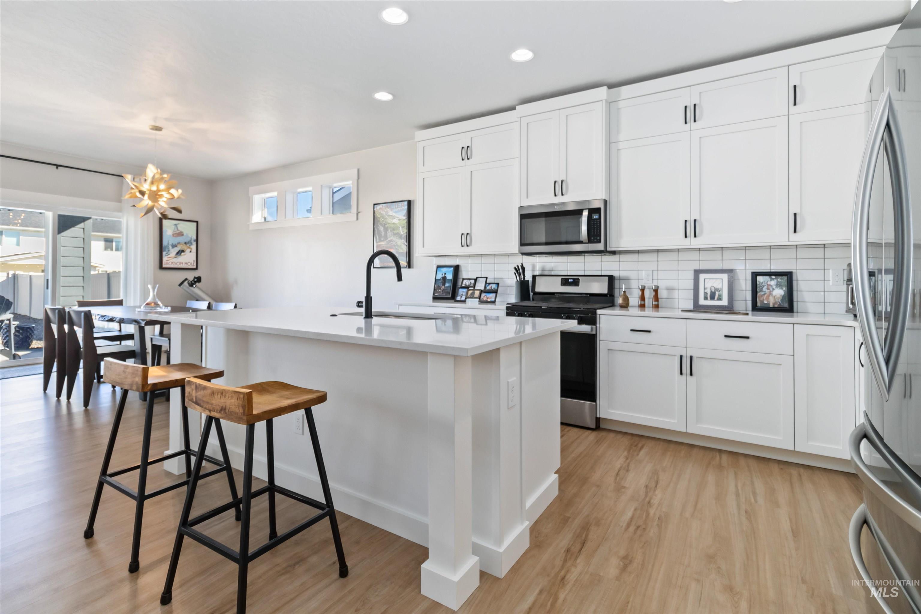 Kitchen with stainless steel appliances, decorative backsplash, white cabinetry, light wood-type flooring, and recessed lighting