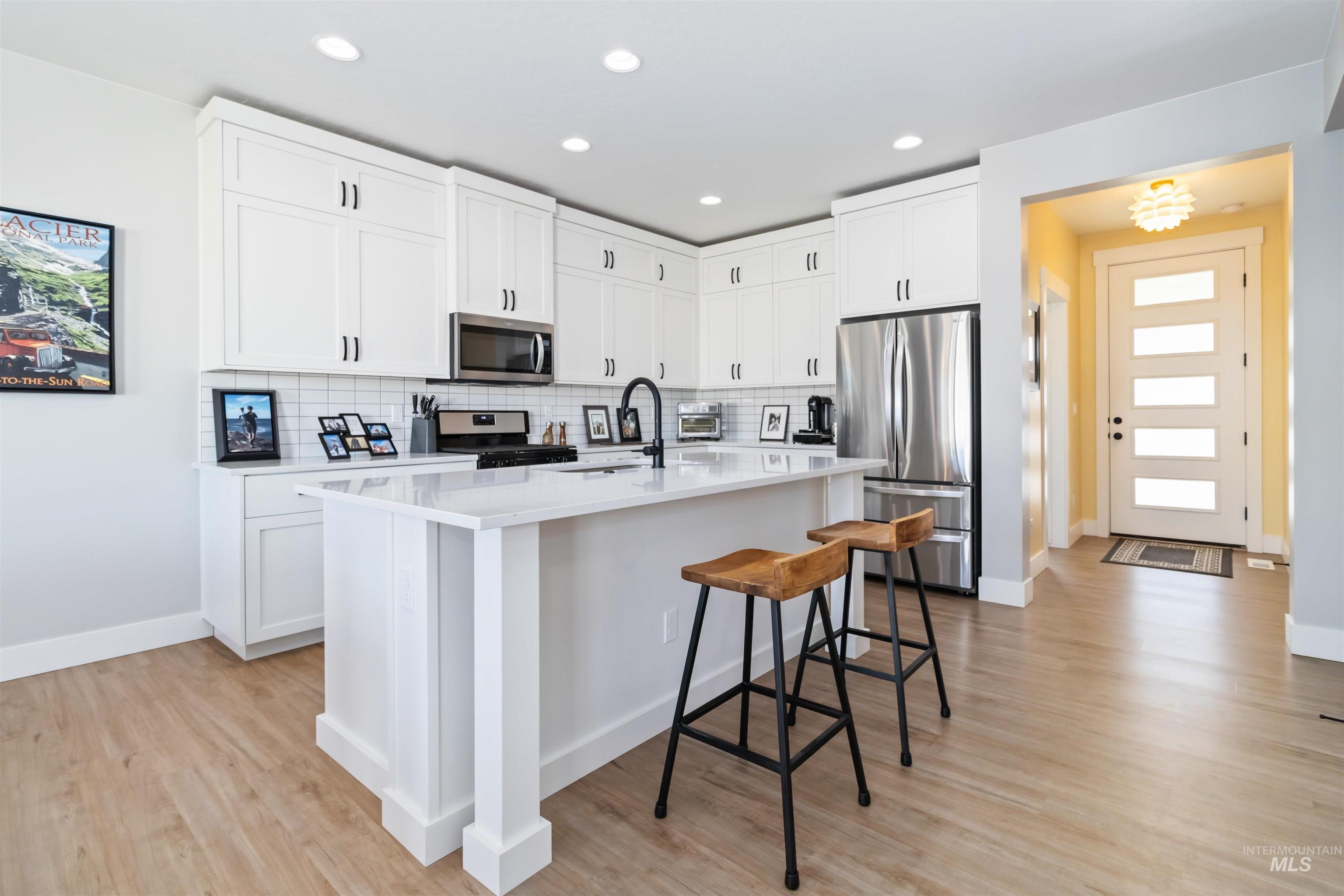 Kitchen with stainless steel appliances, white cabinetry, a kitchen bar, tasteful backsplash, and recessed lighting