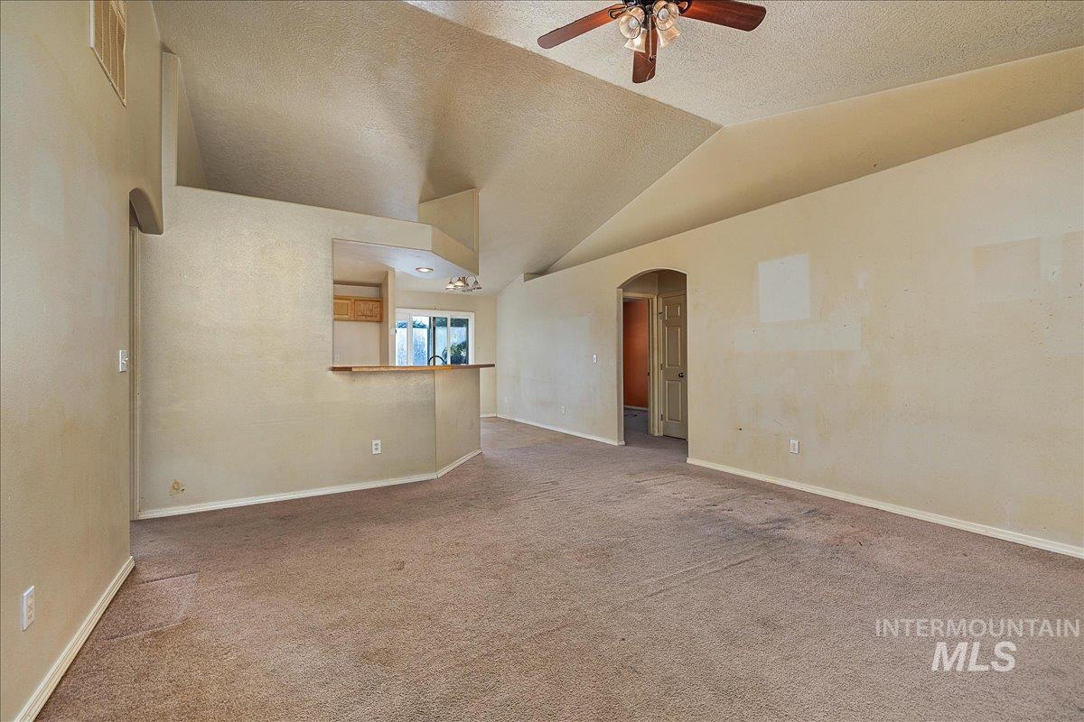 Unfurnished living room featuring arched walkways, a textured ceiling, carpet flooring, a ceiling fan, and lofted ceiling
