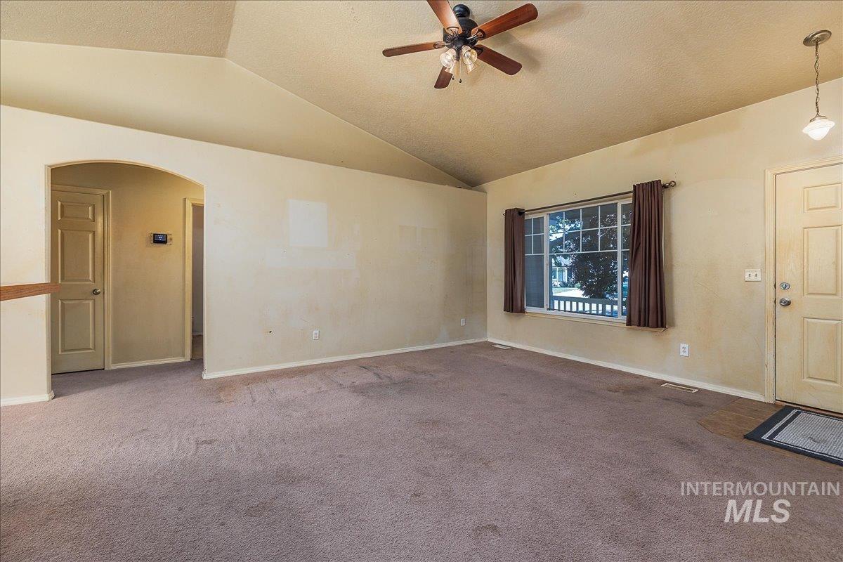Carpeted empty room featuring vaulted ceiling, a ceiling fan, arched walkways, and a textured ceiling