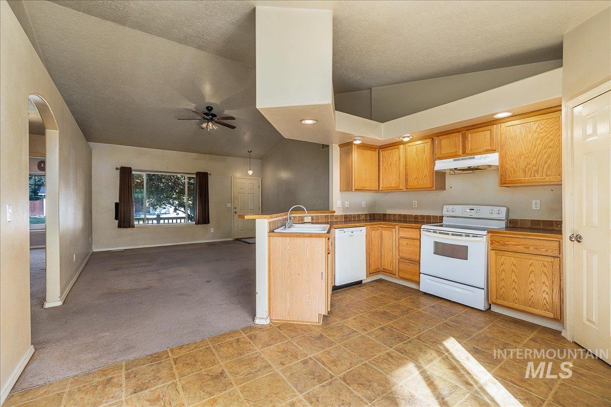 Kitchen featuring white appliances, lofted ceiling, a peninsula, open floor plan, and a ceiling fan