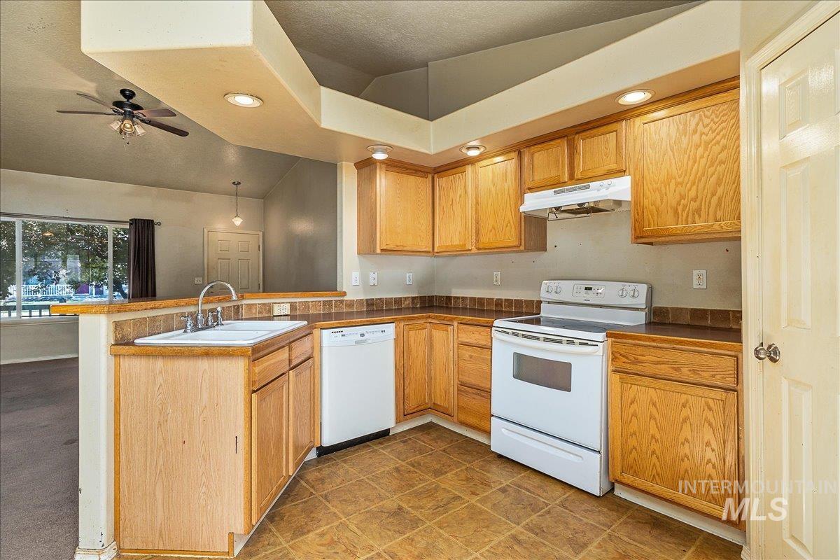 Kitchen with a peninsula, white appliances, recessed lighting, under cabinet range hood, and vaulted ceiling