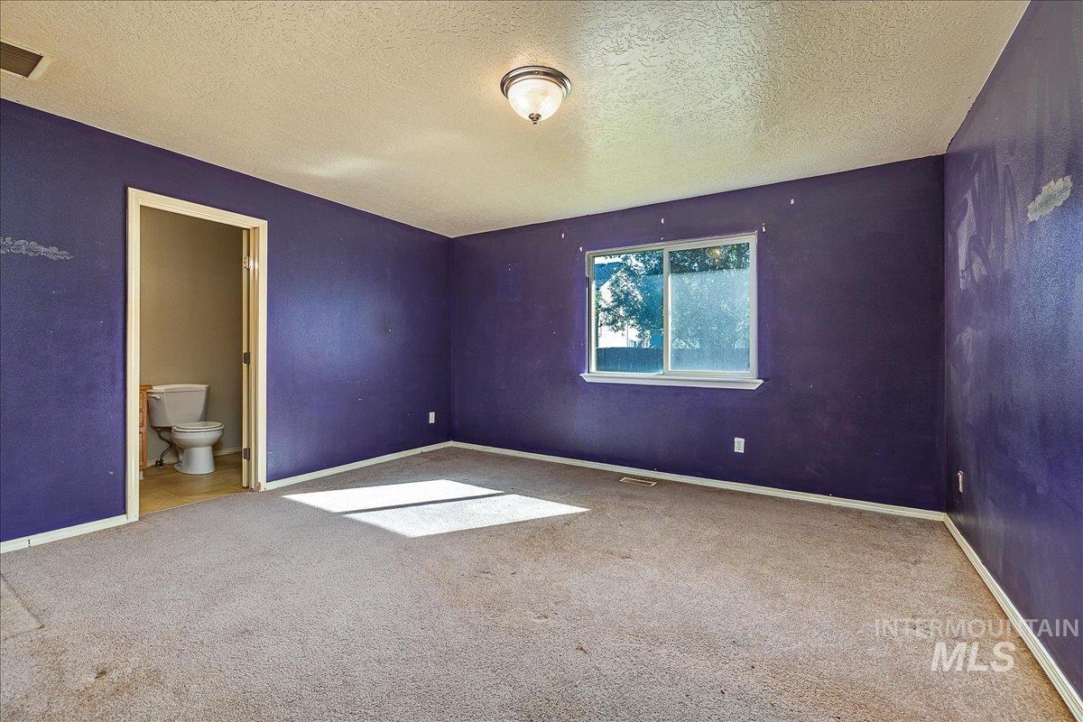 Unfurnished bedroom featuring a textured ceiling, light colored carpet, and ensuite bath
