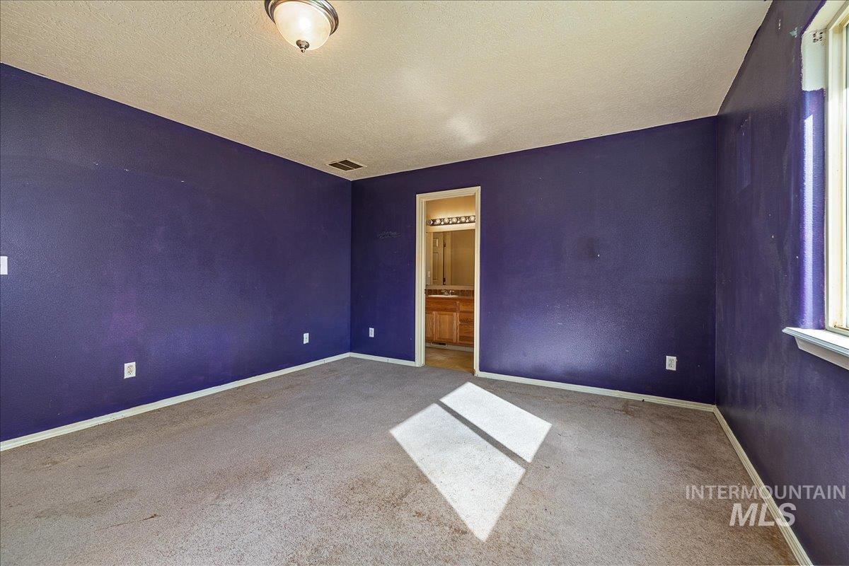 Unfurnished bedroom featuring a textured ceiling, ensuite bathroom, and carpet floors