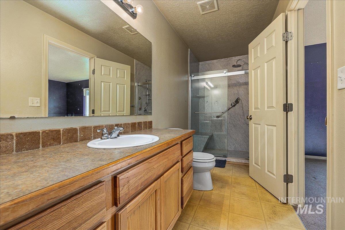 Bathroom featuring a stall shower, vanity, a textured ceiling, and light tile patterned floors