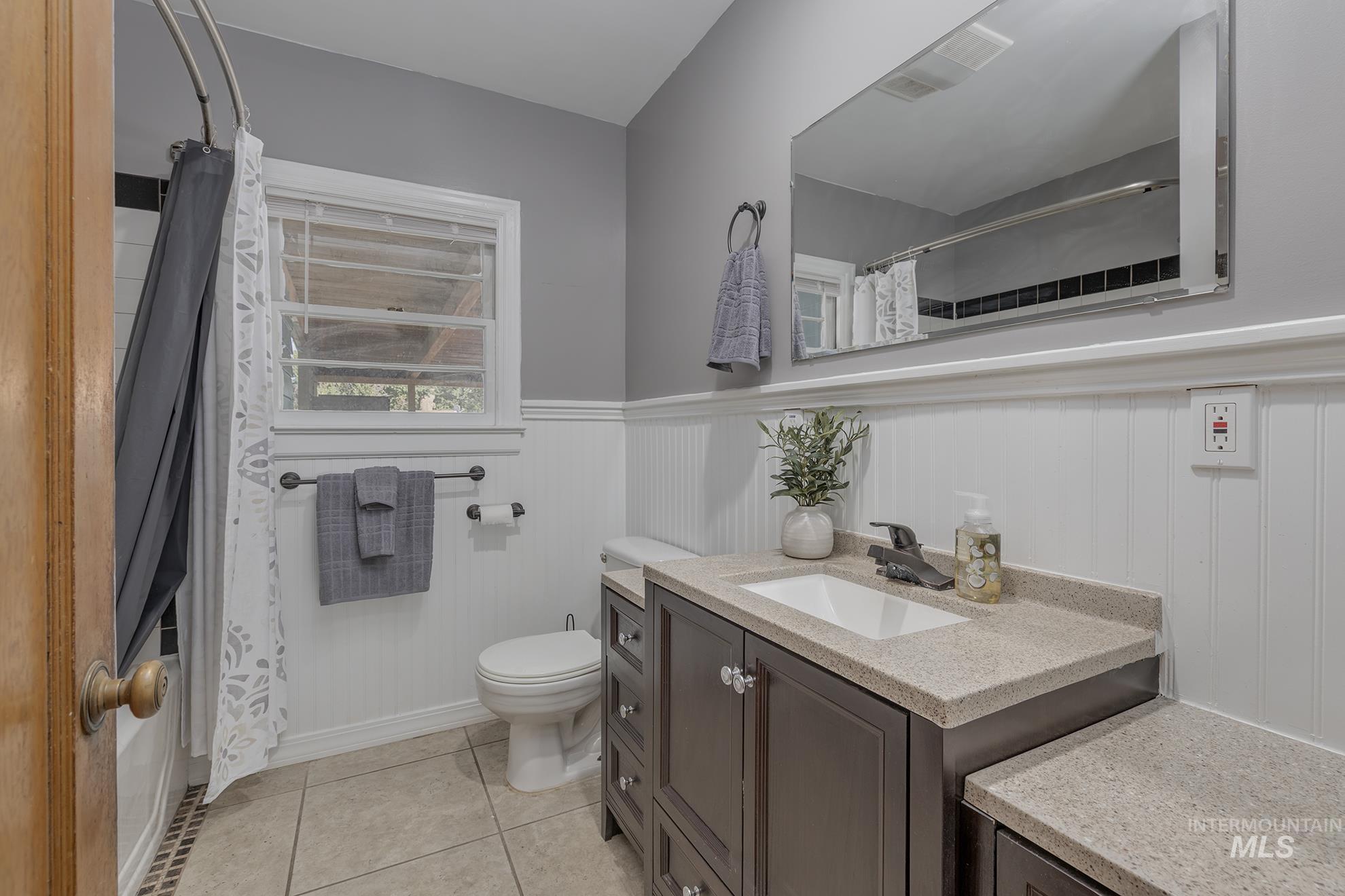 Full bath with vanity, light tile patterned floors, shower / bath combo, and wainscoting