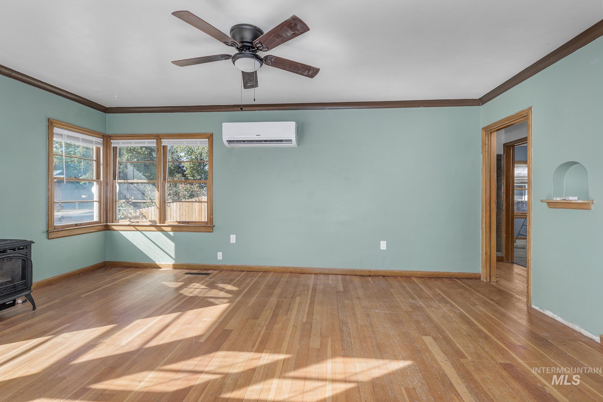 Empty room with crown molding, wood finished floors, a wood stove, and a ceiling fan