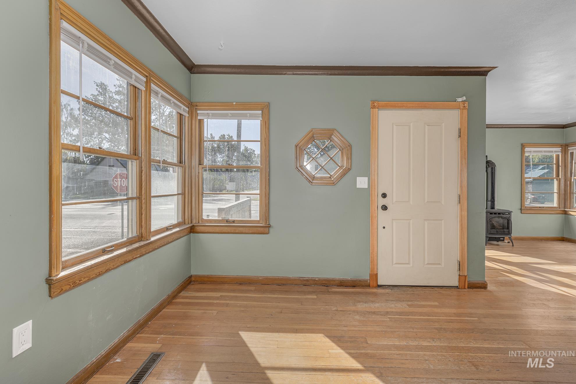 Entryway with crown molding, light wood-style floors, and a wood stove