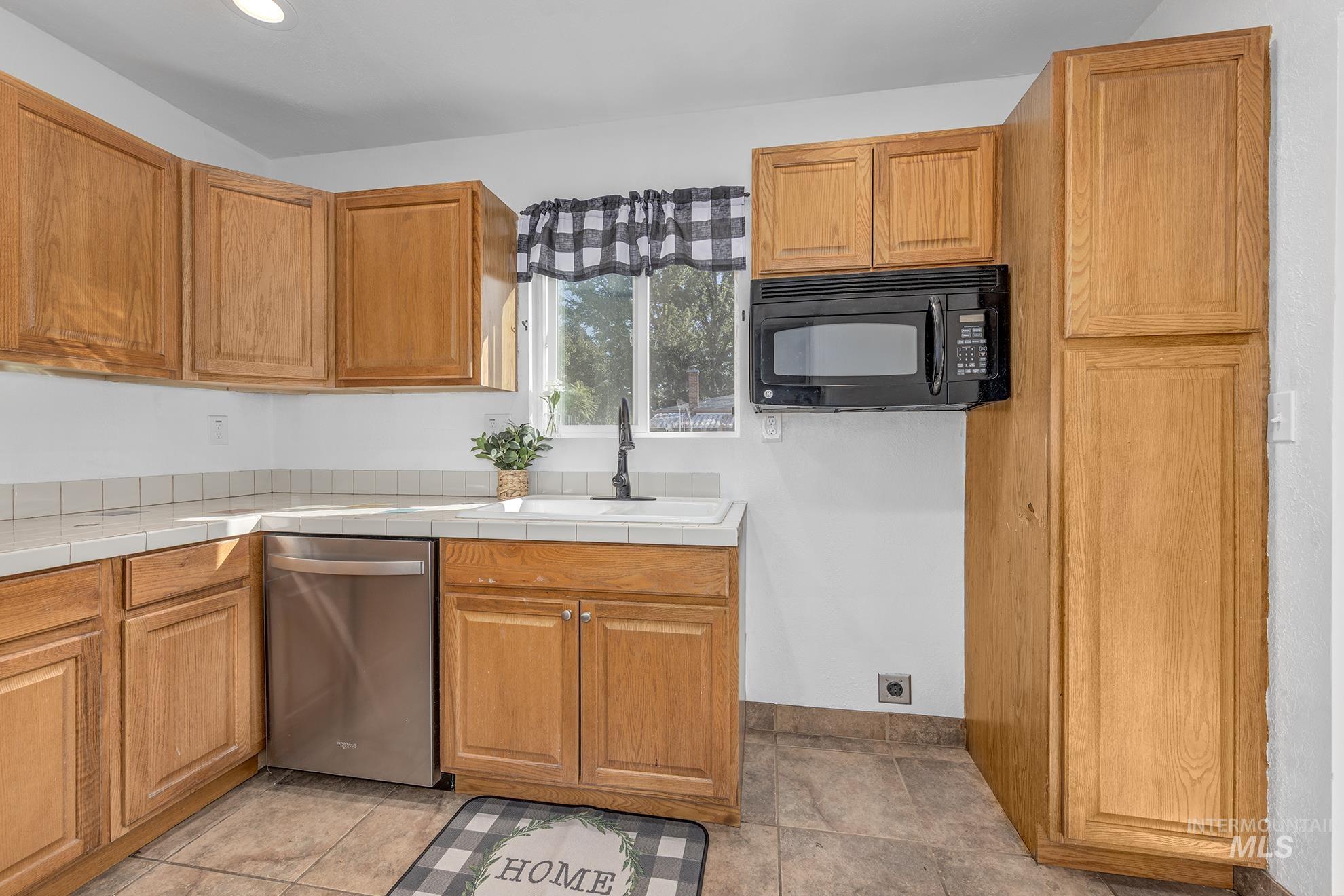 Kitchen featuring dishwasher, black microwave, tile countertops, brown cabinetry, and recessed lighting