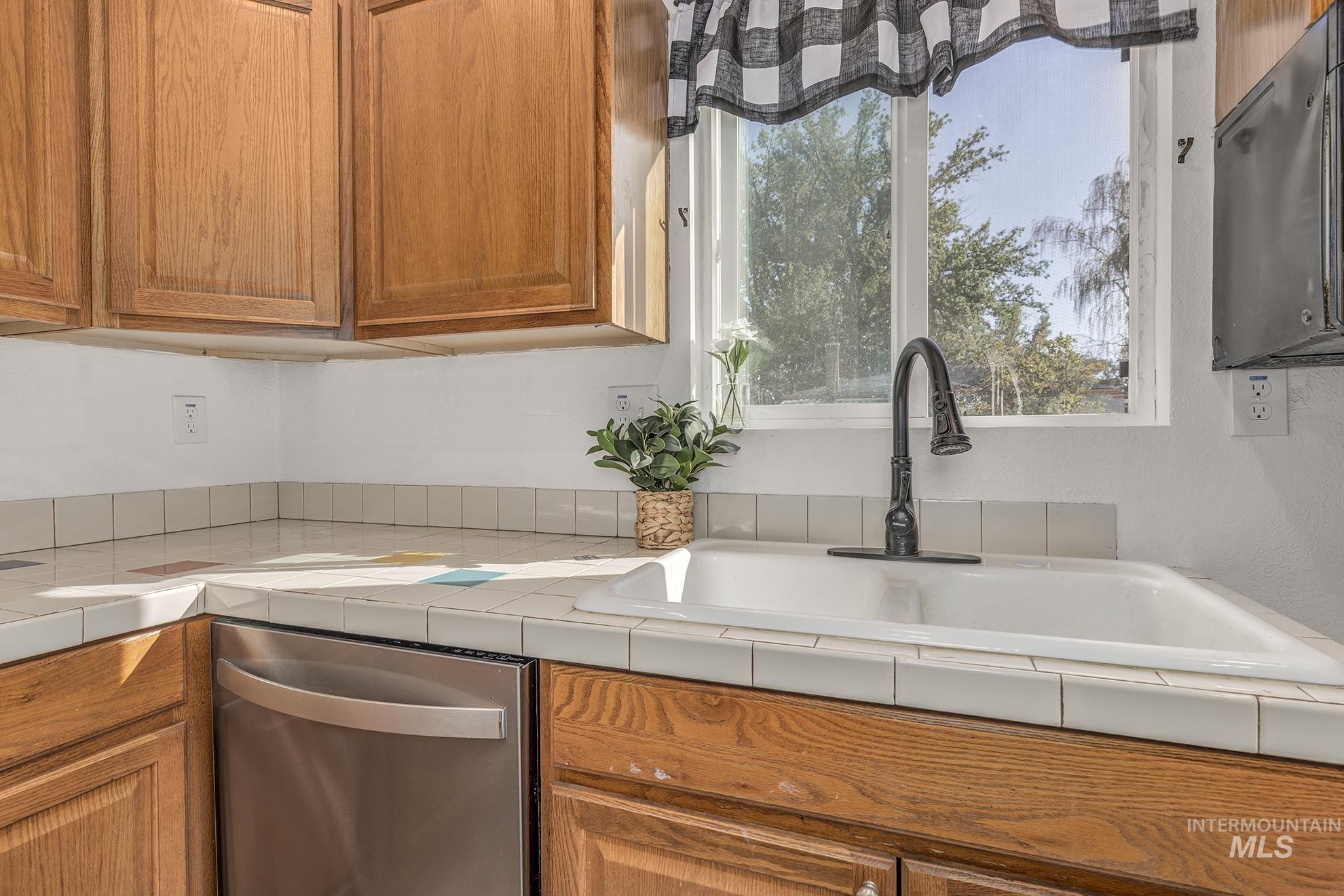 Kitchen featuring stainless steel dishwasher, brown cabinetry, and tile countertops