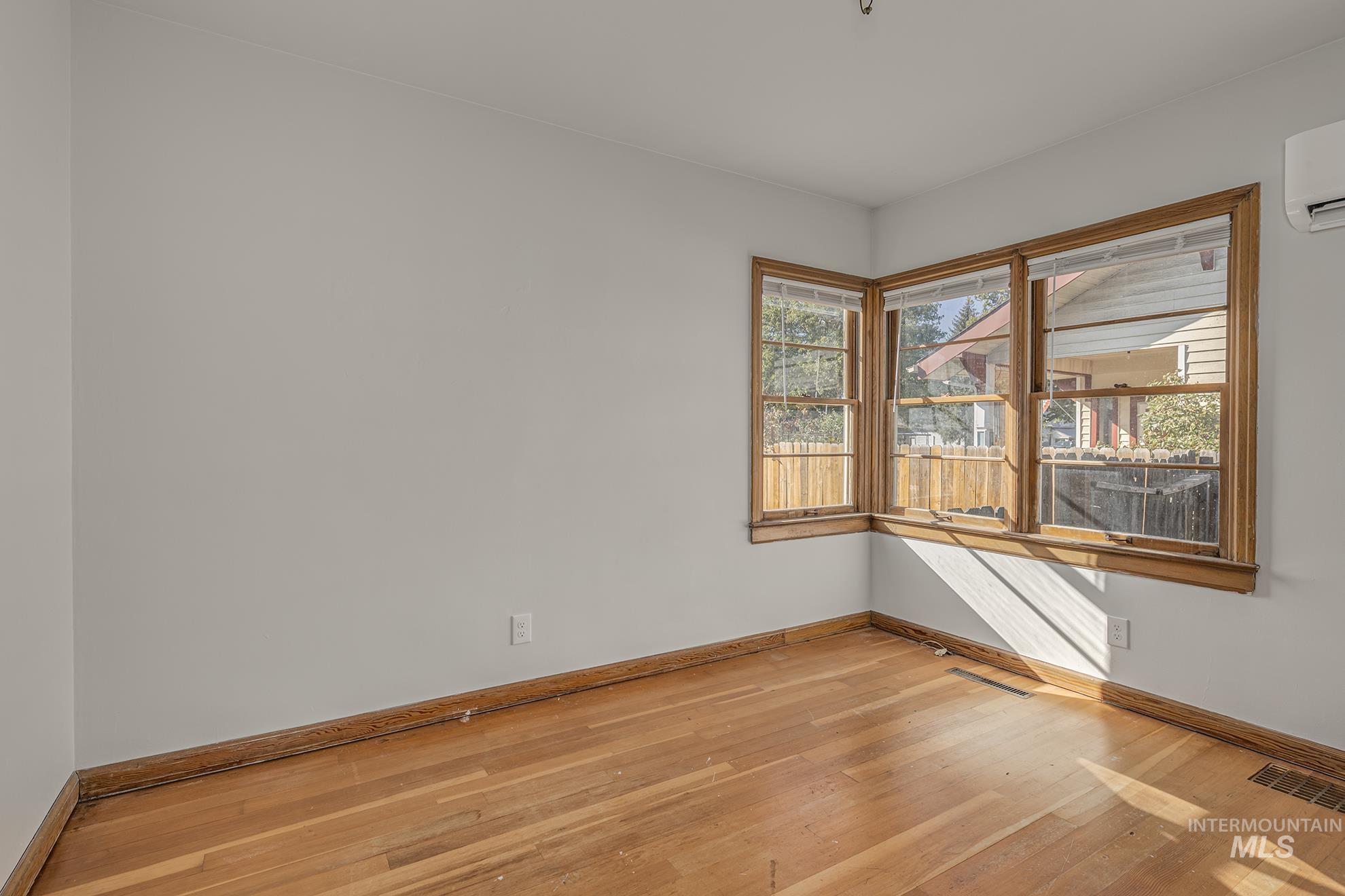 Empty room featuring light wood-style flooring and a wall mounted air conditioner